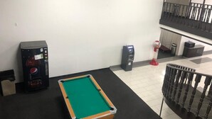 A pool table in a room with a white wall and a black floor. There are vending machines and a trash can visible. - Shadeland Inn Indianapolis (Indianapolis)