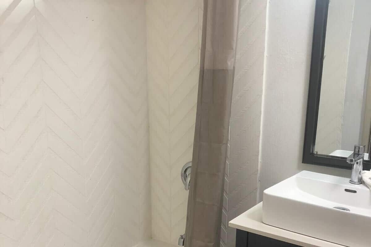 A bathroom with a white herringbone-patterned wall, a white bathtub, a glass shower enclosure, and a black vanity with a white sink.
