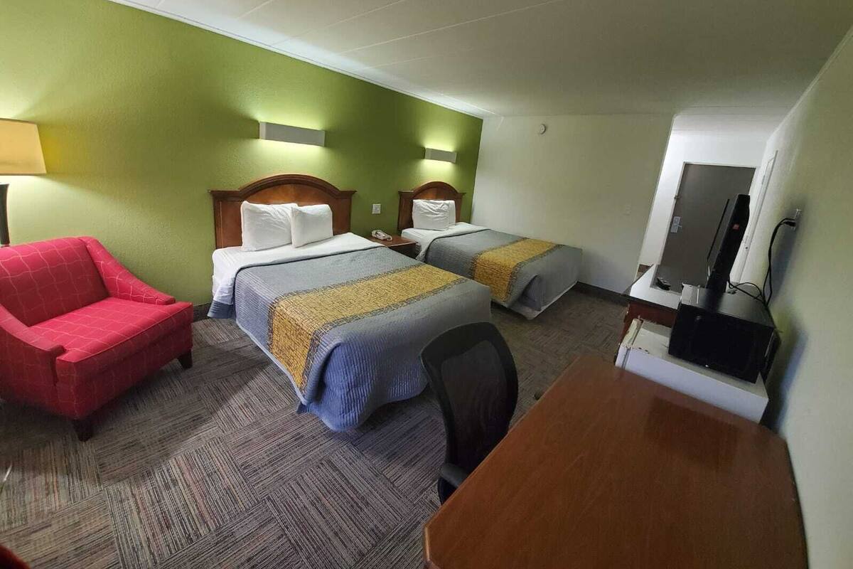 A hotel room with two beds, a red armchair, a desk, and a television.