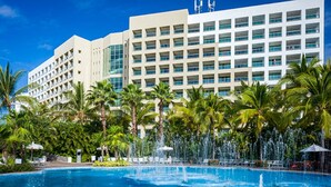 Un hôtel doté d’une piscine, de palmiers et d’une fontaine.