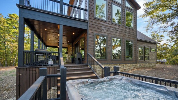 Een modern huis met twee verdiepingen, met een hottub op het terras, een overdekte zitplek en een stenen fundering.
