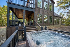 A modern two-story house with a hot tub on the deck, a covered outdoor seating area, and a stone foundation.