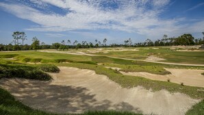 En golfbane med sandbunkere, grønne fairways og træer under en let skyet himmel.