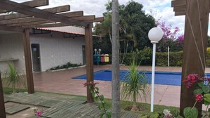 Una pérgola de madera, una piscina y un pequeño jardín con plantas y flores.