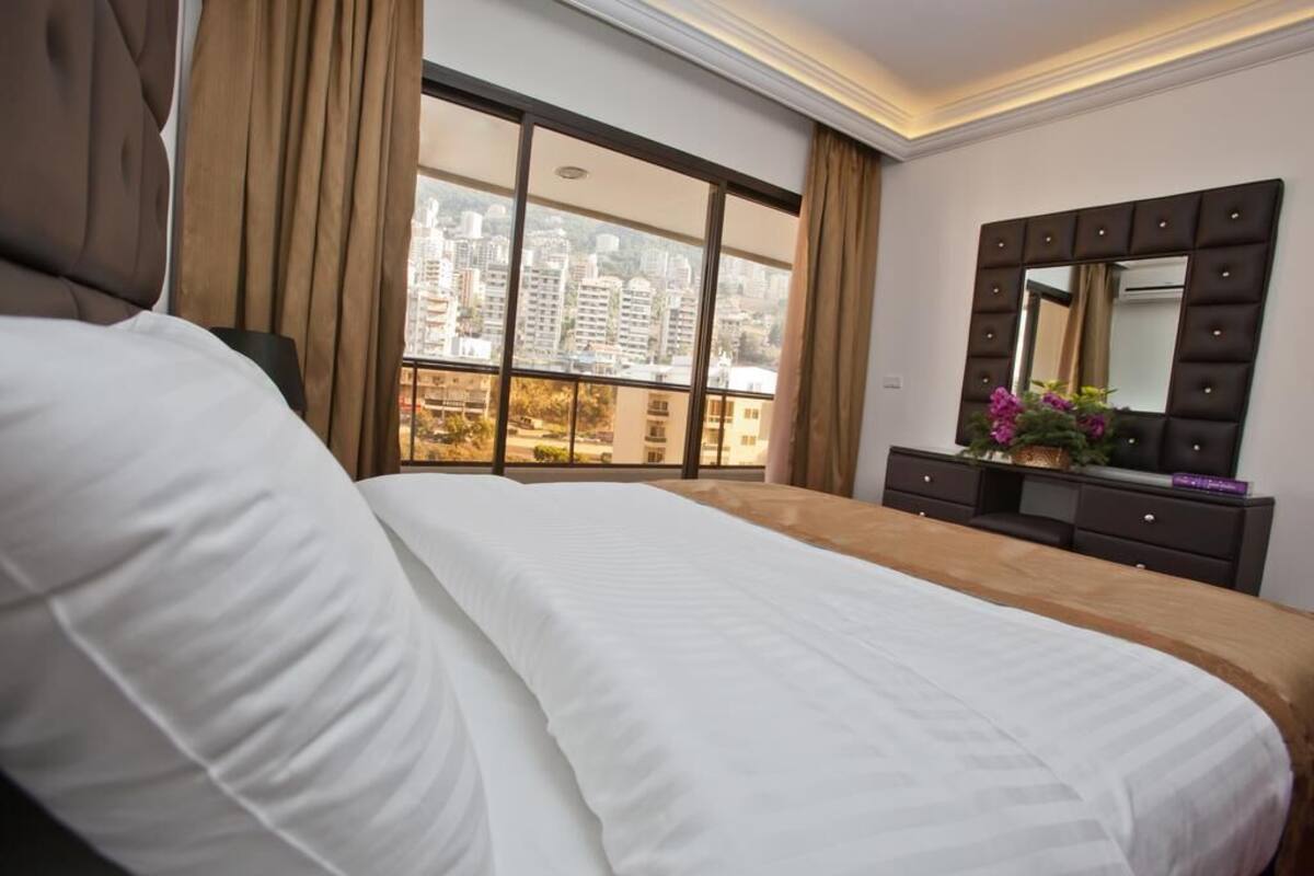 A hotel room with a large bed, a dresser, a mirror, and a window with a city view.