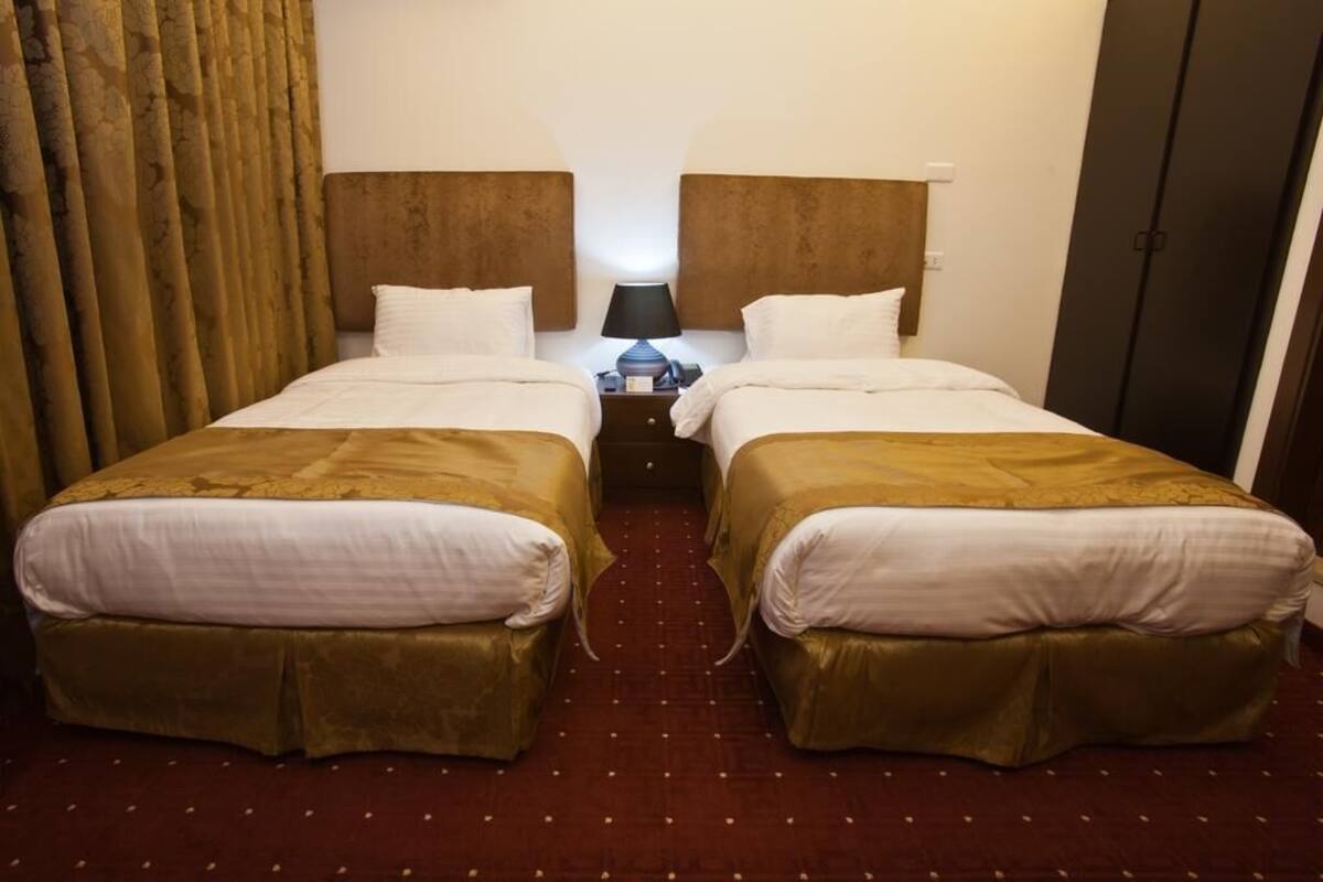 A hotel room with two beds, a nightstand with a lamp, and a wardrobe.