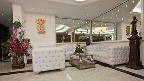 Eine Lobby mit weiß gepolsterten Sofas, einem Glastisch und einem großen Spiegel, der den Innenraum widerspiegelt.
