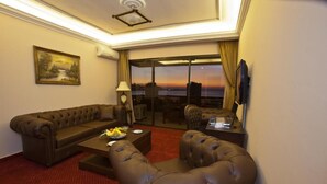 Ein Hotelzimmer mit Ledersofa, einem Couchtisch und Blick auf die Skyline bei Sonnenuntergang.