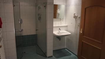 Un baño con ducha de vidrio, un lavamanos con espejo y una puerta de madera.