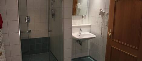 Un baño con ducha de vidrio, un lavamanos con espejo y una puerta de madera.