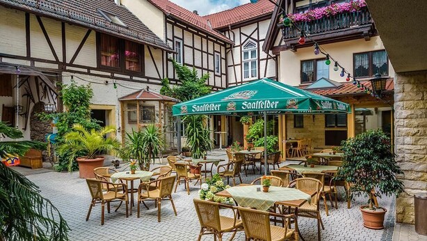 A courtyard with outdoor seating, potted plants, and a green umbrella with 'Saafelber' branding.