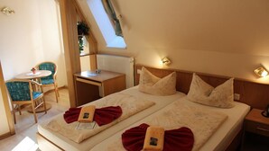 A room with two beds, a small desk, a chair, and a window.