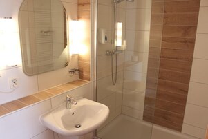 Casa de banho com lavatório branco, espelho e cabine de duche com parede de vidro.