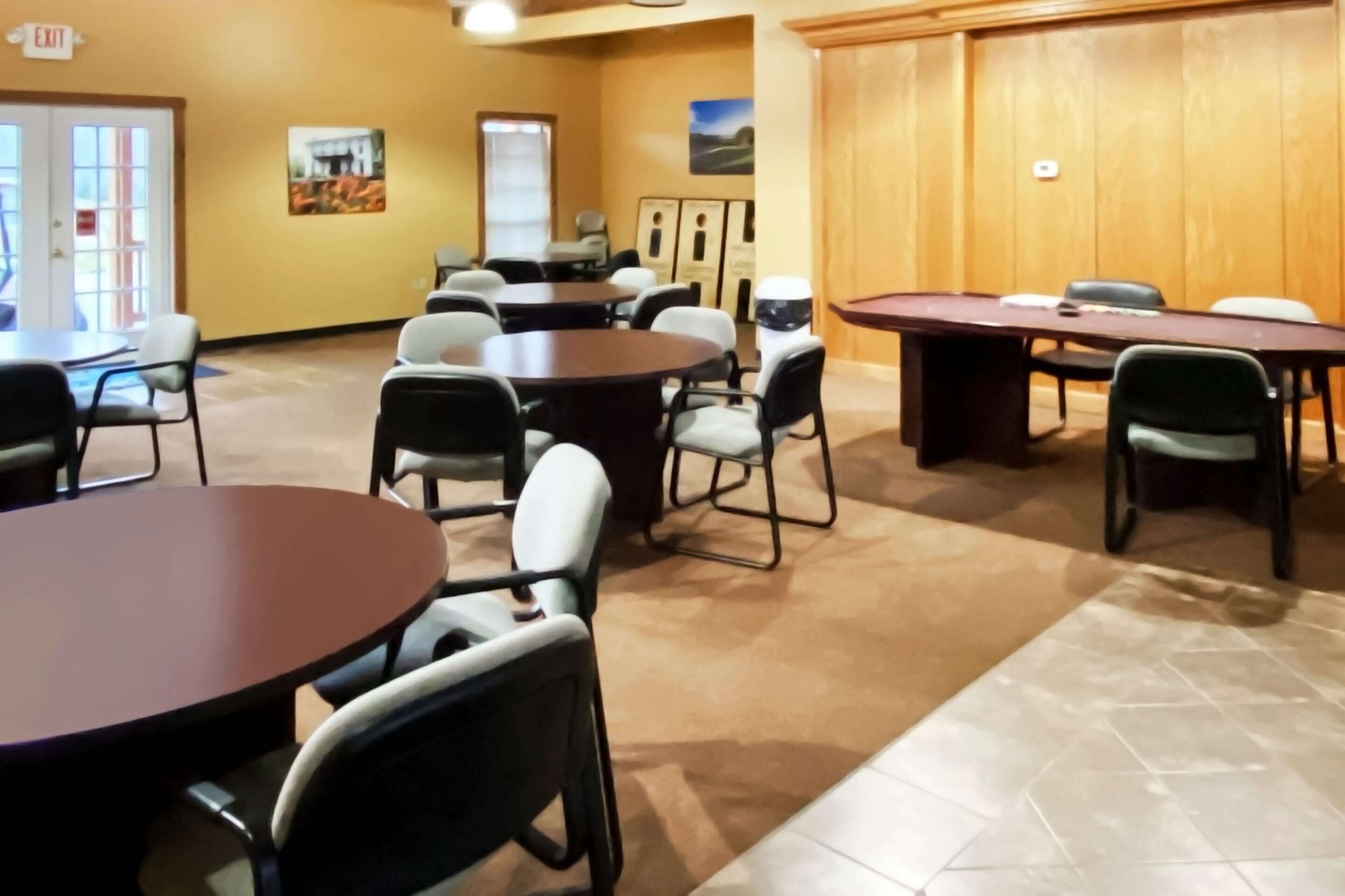 A conference room with multiple tables and chairs, a wooden paneled wall, and a door marked "EXIT".