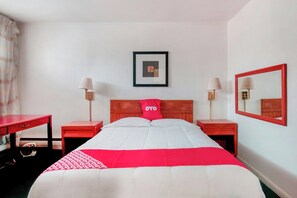 Una habitación de hotel con cama, dos mesitas de noche, escritorio, silla, espejo y un cuadro en la pared.