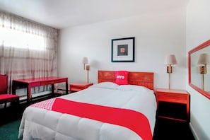Habitación de hotel con cama, escritorio, dos mesitas de noche, espejo, ventana con cortinas e imagen enmarcada en la pared.