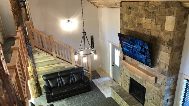 Un vaste espace de vie agrémenté d’une cheminée en pierre, d’un canapé en cuir noir et d’un escalier en bois.