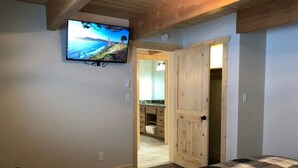 Une chambre à coucher avec un lit, un téléviseur fixé au mur et une porte en bois donnant sur une salle de bain.