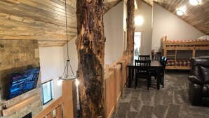 Une pièce confortable de style loft, avec une cheminée en pierre, une table à manger en bois et un lit superposé.