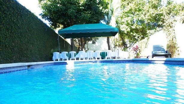A swimming pool with a green canopy and white lounge chairs. - Hotel El Torogoz (San Salvador)