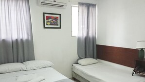 A hotel room with two beds, a window with curtains, an air conditioner, and a framed picture on the wall. - Hotel El Torogoz (San Salvador)