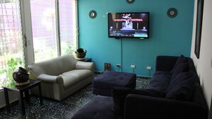 A living room with a beige sofa, a dark blue couch, and a television displaying a football game. - Hotel El Torogoz (San Salvador)