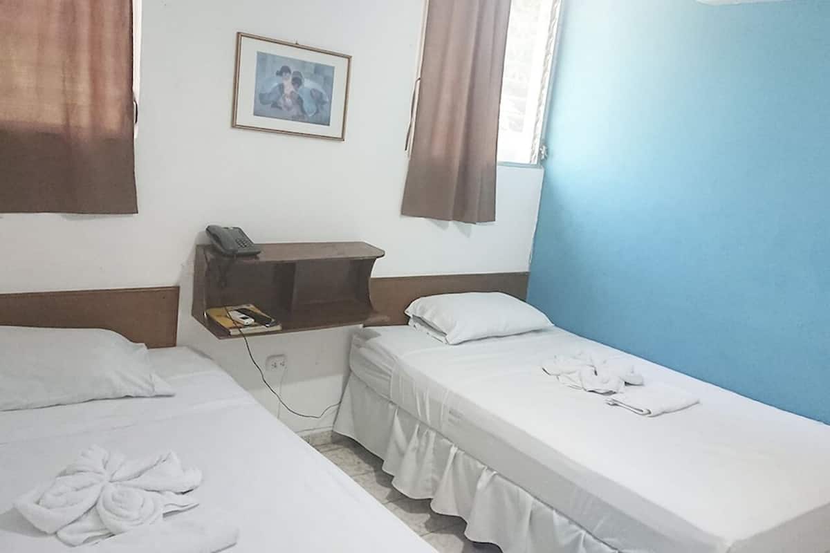 Une chambre d’hôtel avec deux lits, une table de chevet avec un téléphone, un tableau encadré au mur et une fenêtre avec des rideaux.
