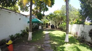 A backyard with a stone pathway, palm trees, and a barbecue area. - Hotel El Torogoz (San Salvador)