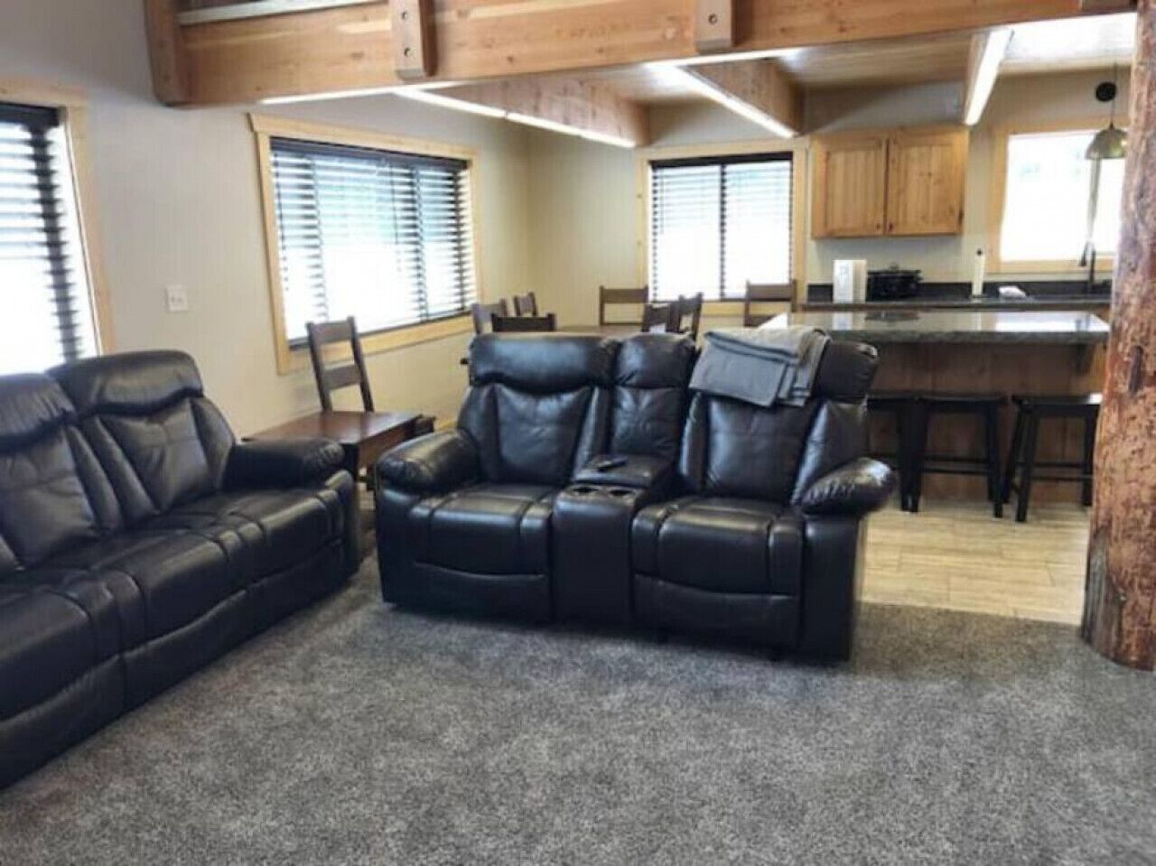 A living room with a black leather sofa and a dining area with wooden cabinets and a kitchen in the background.