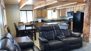 Una sala de estar acogedora con un sofá de cuero y un sillón reclinable, un comedor con mesa y sillas, y una cocina con armarios de madera y electrodomésticos.