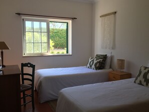 A room with two beds, a chair, a desk, and a window with a view of greenery. - House - Holiday Home (Olhão)