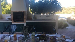An outdoor dining area with a brick oven, a table set with plates, glasses, and food. - House - Holiday Home (Olhão)
