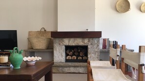 A cozy living room with a stone fireplace, a wooden table, two chairs, a green vase, and a woven basket. - House - Holiday Home (Olhão)