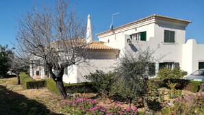 A white building with a tiled roof, a white tower, and a garden with pink flowers. - House - Holiday Home (Olhão)