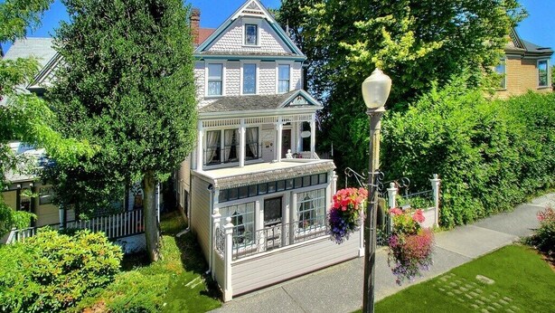 Una casa de estilo victoriano con un porche delantero destacado, un vestíbulo cubierto y un jardín bien cuidado con césped y parterres de flores.