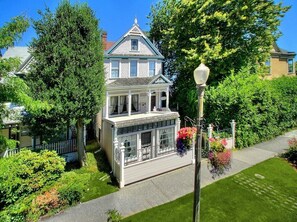 A Victorian-style house with a prominent front porch, a covered front entrance, and a well-maintained garden with a lawn and flower beds.
