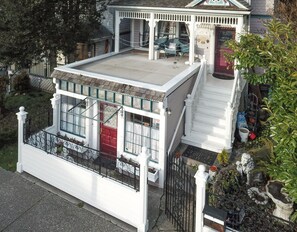 Una casa de dos pisos con balcón, puerta roja y un pequeño porche.
