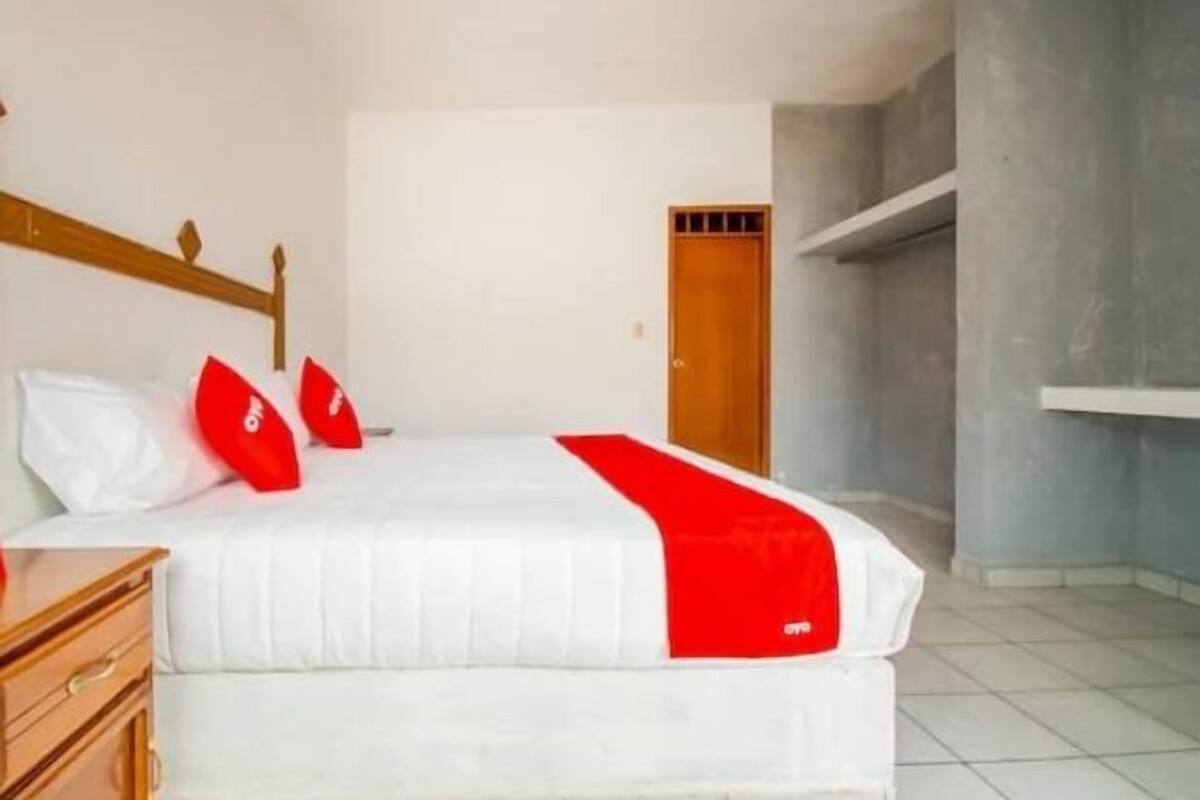 A bedroom with a bed, wooden headboard, white walls, a wooden door, and a tiled floor.