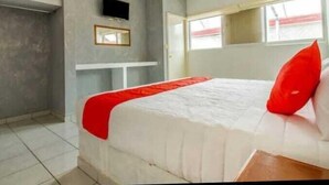Un dormitorio con una cama, un televisor montado en la pared y una ventana.