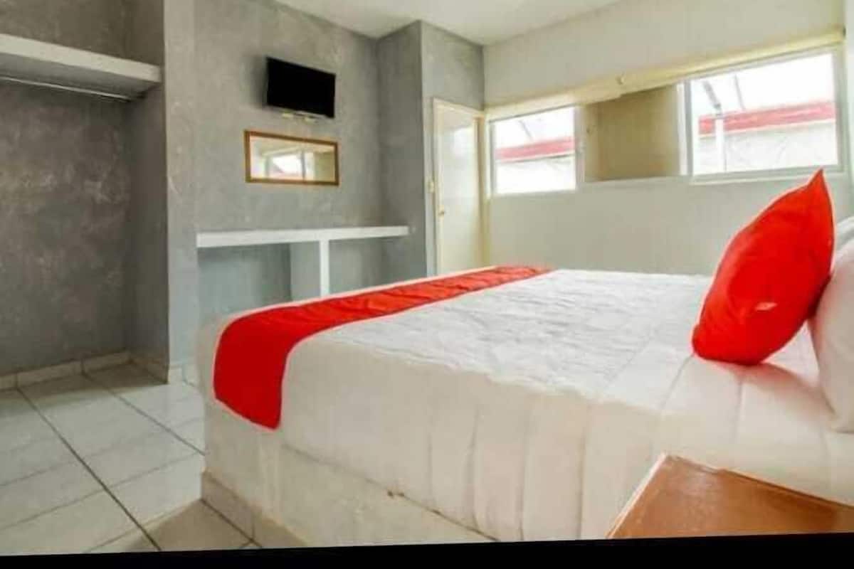 A bedroom with a bed, a TV mounted on the wall, and a window.