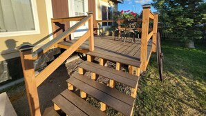 A wooden deck leading to a house with a white door and windows. - Glacier Corner: Enhance Your Adventure (East Glacier Park Village)