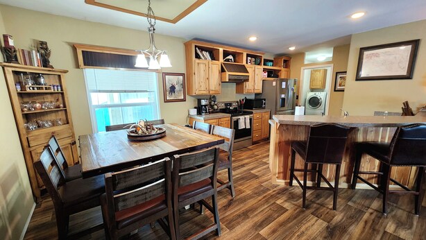A kitchen with wooden cabinets, a dining table with chairs, and a bar area. - Glacier Corner: Enhance Your Adventure (East Glacier Park Village)