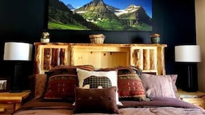 A bedroom with a bed, pillows, a TV mounted on the wall, and a wooden console table. - Glacier Corner: Enhance Your Adventure (East Glacier Park Village)