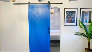 Una habitación con una puerta corrediza azul de estilo rústico, un candelabro, obras de arte enmarcadas y una planta en maceta.