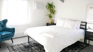 Un dormitorio moderno con una cama grande, un sillón azul, una planta en maceta y una mesita de noche.