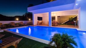 Et moderne hus med swimmingpool, udendørs møbler og en trappe til en etage over.