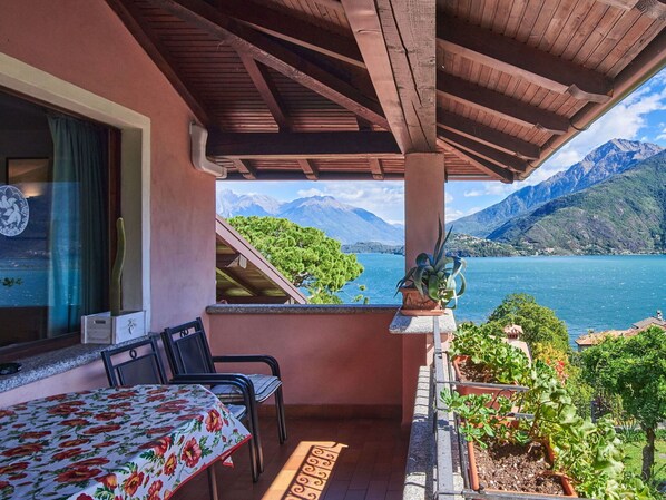 A balcony with a table and chairs, a potted plant, and a view of a lake and mountains.