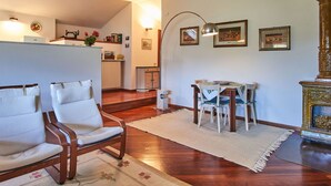 A spacious living room with a wooden floor, two white armchairs, a dining table with chairs, and a decorative fireplace. - Lovely apartment for 5 guests with A/C, WIFI and balcony (Musso)