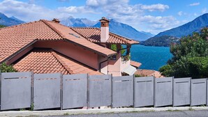 A house with a red-tiled roof, a balcony, and a view of a lake and mountains. - Lovely apartment for 5 guests with A/C, WIFI and balcony (Musso)