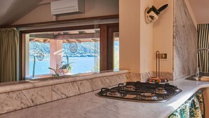 A kitchen with a gas stove, a window with a view of a lake, and a wooden ceiling. - Lovely apartment for 5 guests with A/C, WIFI and balcony (Musso)